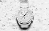 A white Swatch x Omega Bioceramic Moonswatch Mission To Moonphase Snoopy watch is placed on a sandy surface, resembling the moon's surface, with paw prints visible. Náhľad obrázku produktu