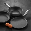 Three frying pans and two eggs are arranged on a dark, textured surface. Náhled obrázku produktu