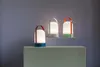 Three modern LED lanterns with colored bases and handles are displayed on tiered platforms against a purple background. Náhled obrázku produktu