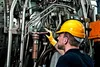 A person in a yellow hard hat and yellow gloves is inspecting complex machinery. Produktbild-Vorschau