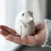 A small white ceramic hedgehog figurine is held in a person's open palm. Produktbild-Vorschau