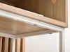 A close-up view of the underside of a shelf on a piece of furniture, showing the white metal frame and the wood-grain shelf. Náhled obrázku produktu