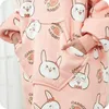 A close-up view of a person wearing a pink hoodie blanket with a repeating pattern of cartoon rabbits and carrots. Náhled obrázku produktu