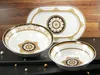 A set of three white porcelain serving dishes with gold and black ornate detailing, arranged on a dark surface with a wooden background. Produktbild-Vorschau