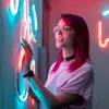 A young woman with pink hair interacting with neon lights. Produktbild-Vorschau