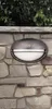 An outdoor wall light mounted on a stone wall, with greenery above. Podgląd zdjęcia produktu