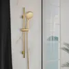 A gold showerhead set mounted on a marble-tiled wall, with a reflection of the showerhead and the outside scenery in a glass panel. Produktbild-Vorschau