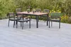 An outdoor dining set with a table and chairs on a patio, surrounded by greenery and flowers. Náhled obrázku produktu