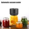 A vacuum sealer is shown on top of a jar filled with yellow fruit, surrounded by other jars filled with jam and pickles. Produktbild-Vorschau