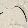 Close-up view of a textured rug with a cream base and black abstract lines. Produktbild-Vorschau