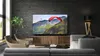 A modern living room with a large TV displaying a paragliding scene, two armchairs, and a sofa. Produktbild-Vorschau