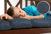 A young boy is lying on a cushioned bench, resting his head on his arms. A close-up inset shows the texture of the cushion fabric. Produktbild-Vorschau