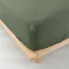 A close-up view of a green fitted sheet on a wooden bed frame. Náhled obrázku produktu