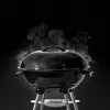 A black charcoal grill with smoke rising from the lid, set against a black background. Náhľad obrázku produktu
