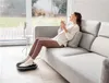 A woman is relaxing on a sofa with a cup of coffee while using a foot massager. Produktbild-Vorschau