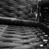 A close-up, black and white view of the woven texture of an outdoor furniture set, focusing on the corner of a chair and the seat. Produktbild-Vorschau