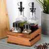 A set of oil and vinegar bottles and salt and pepper shakers in a wooden holder, with a cutting board and a plant in the background. Produktbild-Vorschau