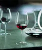 A close-up shot of a wine glass filled with red wine, with a decanter and another empty wine glass in the background, all placed on a marble countertop. Produktbild-Vorschau
