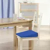 A blue wedge seat cushion is placed on a wooden chair next to a wooden dining table. Produktbild-Vorschau
