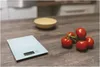 A kitchen scale and a bunch of tomatoes on a wooden table with a bowl in the background. Anteprima dell’immagine prodotto