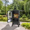 A black gas grill smoker with its door open, filled with food, sits on a patio in a lush garden. Produktbild-Vorschau