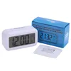 A white digital alarm clock is displayed next to its blue packaging and an instruction manual. Voir les images du produit