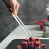 A hand using kitchen tongs to pick up cubes of raw meat. Produktbild-Vorschau