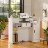 A white reception desk with a computer monitor, drawers, and cabinets, set in a well-lit office or commercial space. Produktbild-Vorschau