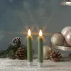Two green LED candles with flickering flames are placed on a surface covered in artificial snow, surrounded by pine branches, pinecones, and Christmas ornaments. Produktbild-Vorschau