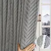 A hand is shown holding a thick, plush, quilted gray curtain. The curtain is partially drawn, revealing a window with a snowy landscape and mountains in the background. Náhled obrázku produktu