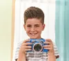 A young boy is smiling and holding a blue toy camera. Podgląd zdjęcia produktu