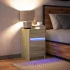 A bedside table with a lamp and books next to a bed. Anteprima dell’immagine prodotto