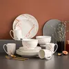 A collection of porcelain tableware with a marble-like pattern and gold accents, arranged on a dark surface against a brown background. Náhled obrázku produktu
