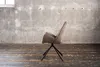 A single chair is shown in a room with a concrete wall and wooden floor. Produktbild-Vorschau