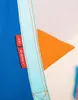 A close-up view of a blue fabric with a light blue trim and two red tags. An orange triangular shape is visible behind the fabric. Náhled obrázku produktu