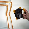 A hand holds a portable LED work light near copper pipes. Produktbild-Vorschau