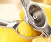 A close-up shot of a silver manual citrus juicer pressing a lemon, with other lemons in the background. Náhľad obrázku produktu