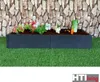 A raised garden bed filled with soil and decorative plants and vegetables, placed on artificial grass in front of a stone-patterned wall. Produktbild-Vorschau