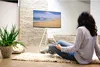 A woman sits on a rug in front of a TV, holding a remote control. Voir les images du produit