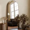A large arched mirror reflects a living room scene with a sofa and window. Decorative items like dried flowers and a small table are also visible. Anteprima dell’immagine prodotto