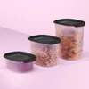 Three clear plastic food storage containers with black lids are arranged on a pink surface. Anteprima dell’immagine prodotto
