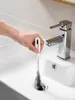A hand is using a drain cleaning brush to remove hair from a sink drain. Produktbild-Vorschau