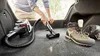 A person is vacuuming the trunk of a car with a Bosch mini vacuum cleaner. Hiking boots are visible next to the vacuumed area. Voir les images du produit