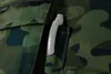 A close-up of a camouflage fabric with a gray plastic handle-like object protruding from a pocket. Náhled obrázku produktu