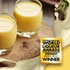 Two glasses of yellow liqueur are shown on a wooden board, with a splash of cream in the foreground and a marketing award overlay. Produktbild-Vorschau