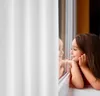 A young girl looks out a window, her reflection visible. Produktbild-Vorschau