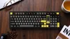 A top-down view of a mechanical keyboard on a wooden desk, with coffee beans, glasses, and a cup of tea. Produktbild-Vorschau