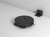 A black robot vacuum cleaner is shown on a white floor next to its charging dock, which is mounted on a white wall. Voir les images du produit