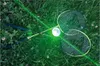 Two badminton rackets and a shuttlecock are lying on the grass, illuminated by a green laser beam. Produktbild-Vorschau