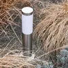 A silver and white outdoor lamp surrounded by dry grass and gravel. Anteprima dell’immagine prodotto